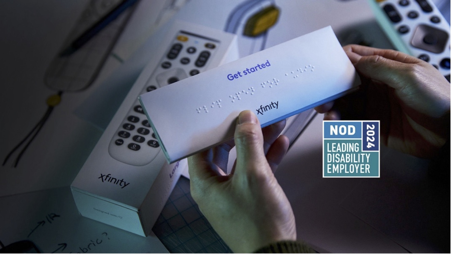 A close-up image of hands holding an Xfinity branded envelope or package with "Get started" printed on it and braille text below. An Xfinity remote control is visible in the background. A "NOD Leading Disability Employer 2024" logo appears in the bottom right corner.